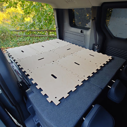 Innenansicht eines KIA PV5 Minicamper mit KIUBIQ Ausbau: Euroboxen und ineinandergreifende helle Holzplatten bilden eine Liegefläche.