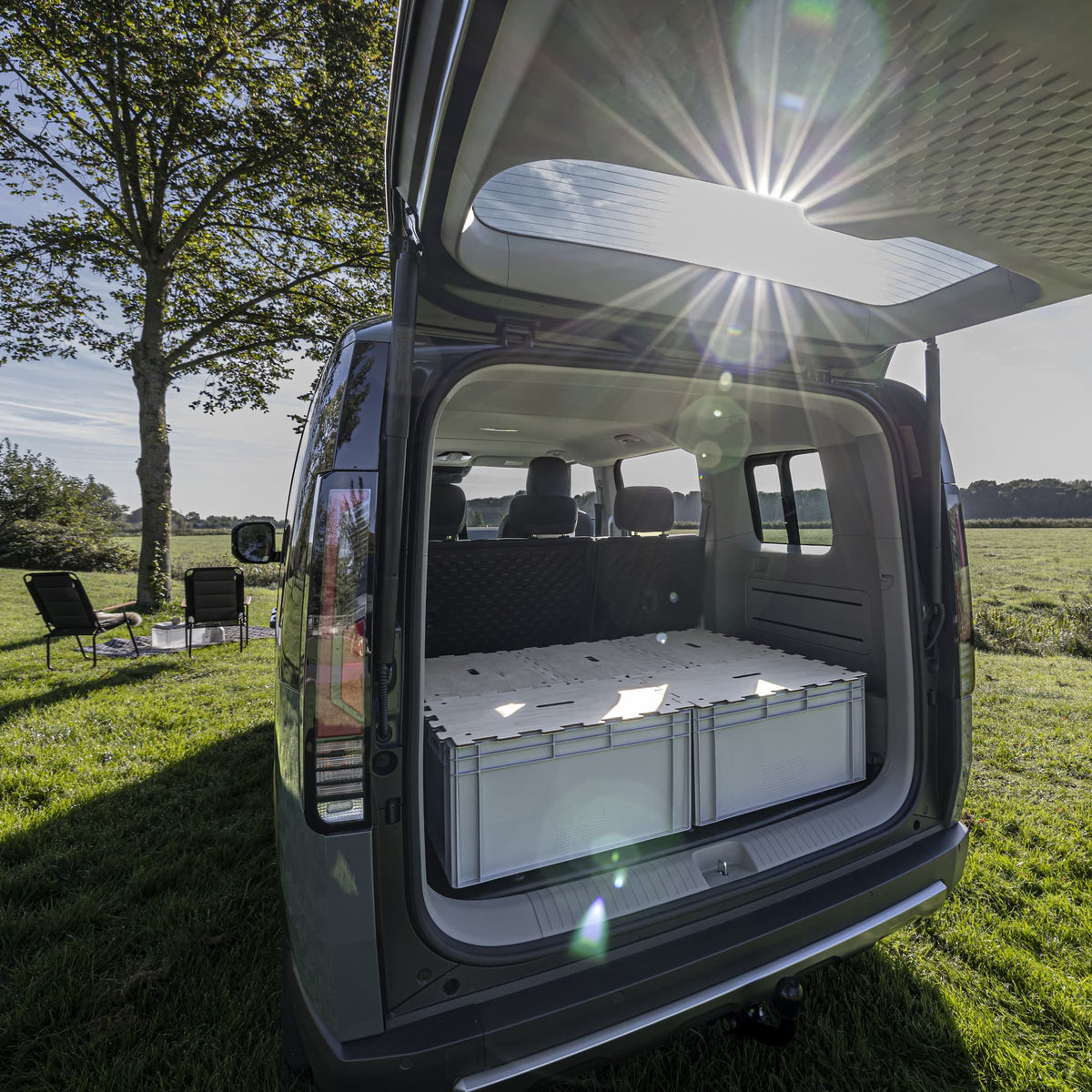 Modularer Kofferraum-Ausbau für KIA PV5: KIUBIQ Eurobox-Bett-System mit hellen Puzzle-Holzdeckeln in der Natur bei Sonnenschein