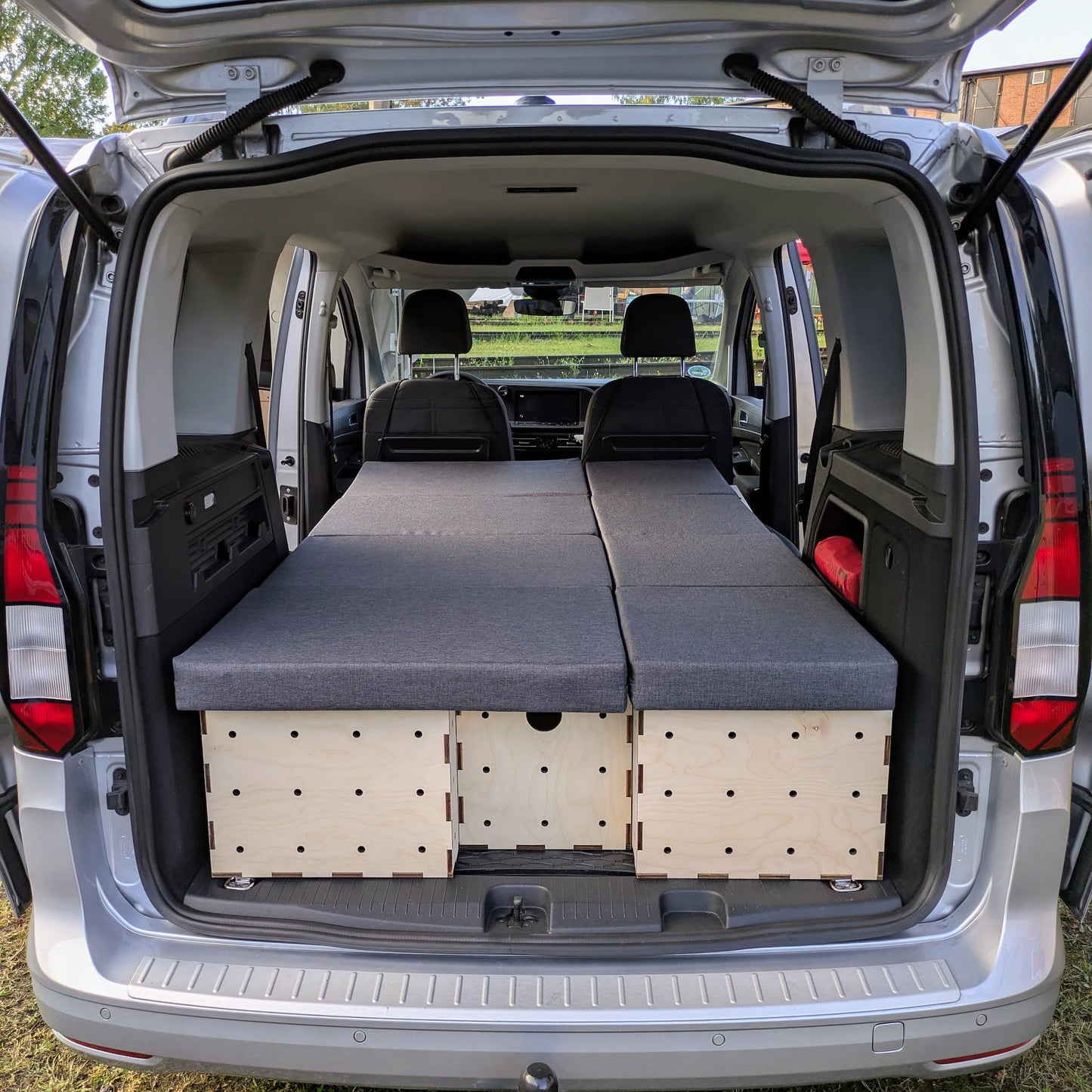 KIUBIQ Caddy Camping Boxen im VW Caddy: modulare Holzboxen mit grauen Polstern in voller Liegeflächen-Konfiguration, Blick durch die Heckklappe.