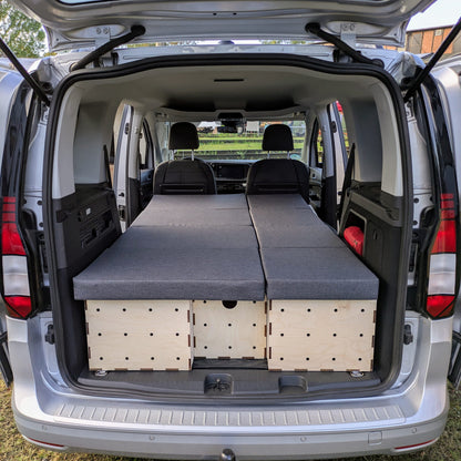KIUBIQ Caddy Camping Boxen im VW Caddy: modulare Holzboxen mit grauen Polstern in voller Liegeflächen-Konfiguration, Blick durch die Heckklappe.