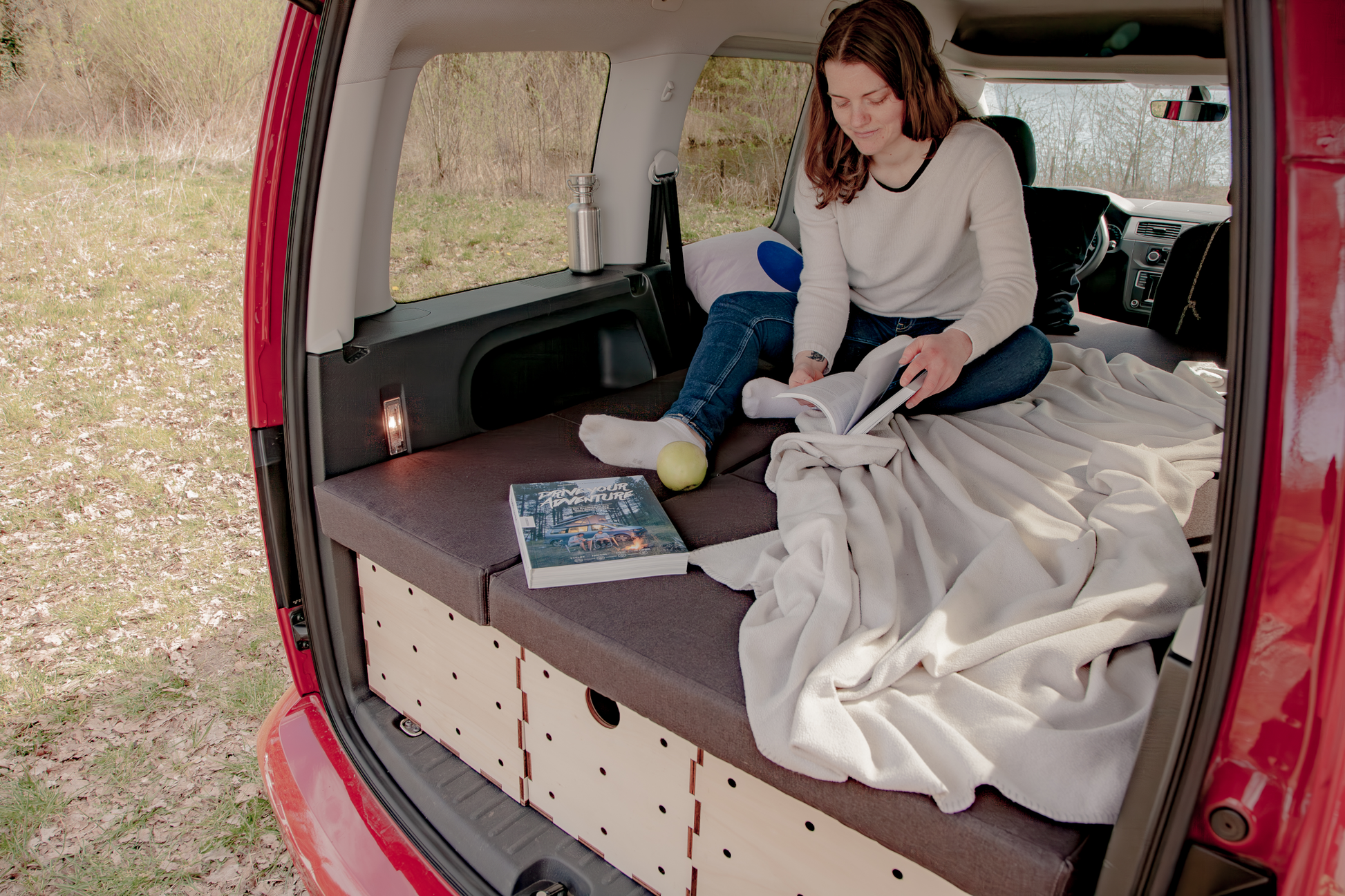 Gemütliche Liegefläche im VW Caddy mit umgeklappten Rücksitzen, ausgestattet mit dem KIUBIQ Camping Set aus unbehandeltem Holz